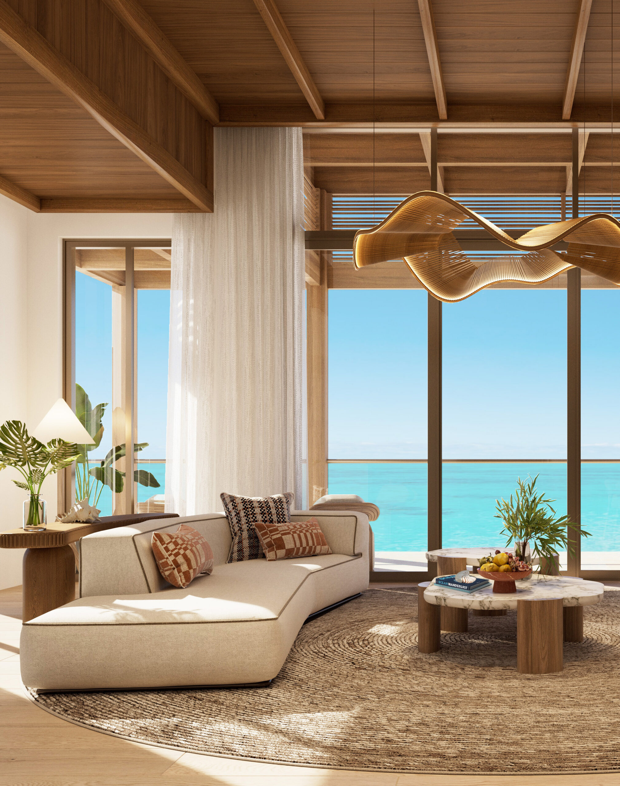 A bright, open luxury living room with cream sectional sofas, a round wood coffee table, a woven area rug, and floor-to-ceiling windows overlooking a turquoise ocean.